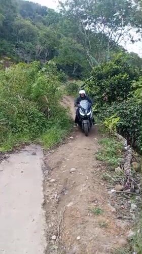 Motorcyclist transitions from dirt path to paved road in Indonesia