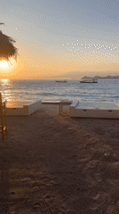 Sunset beach scene with lounge chairs and a traditional boat, Indonesia