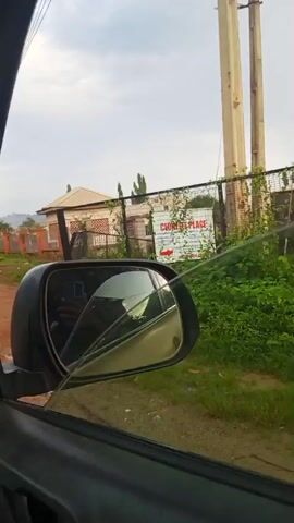 The video shows a street view from inside a vehicle. A sign that reads "CORNELL PLACE" is visible on a fence. A person walks past the fence. The scene appears to be in a residential area with houses and vegetation.
