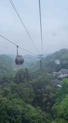 Cable cars navigate misty mountains during rainfall in Yongding District
