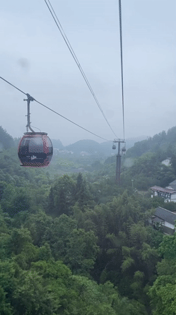 Cable cars navigate misty mountains during rainfall in Yongding District