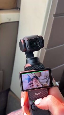 The video shows a person holding a DJI Osmo Pocket camera. The screen displays a selfie of a woman in a white shirt and blue baseball cap, taking a picture with a phone. The camera is recording in 4K30 resolution, with approximately 9 hours and 42 minutes of recording time remaining on the SD card. The camera is held up in what appears to be a vehicle, perhaps a plane or train, given the background panels.