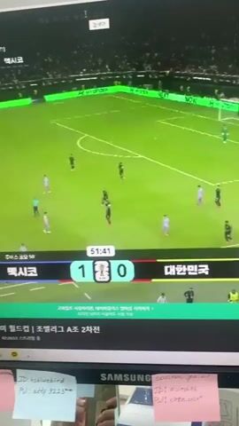 The video shows a computer screen displaying a live soccer match. The score is 1-0 with Mexico leading and South Korea trailing. The time on the clock is 51:42. The game appears to be part of the FIFA World Cup. In the foreground, the bottom edge of the monitor is visible, with several sticky notes attached to it. One note has "hshbluebird" and "PW: atty 9223" written on it. Another note says "ID: olirekas" and "PW: korea 2024". The notes suggest login credentials or passwords.