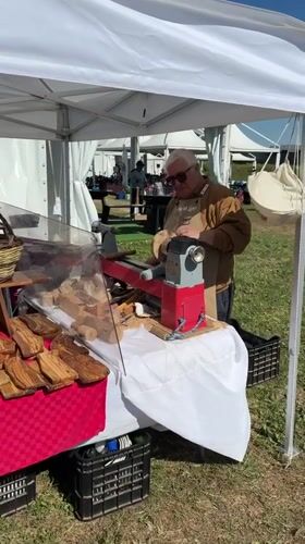 Woodworker demonstrates lathe techniques at outdoor event in Aprilia