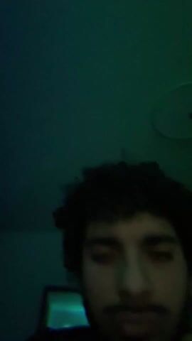 The video begins with a close-up shot of a person's head, mainly focusing on their dark, voluminous hair against a purple background. The lighting shifts to blue, then green, revealing a glimpse of the person's face. The camera then moves towards a computer monitor, which appears to be displaying video editing software with an orange and teal interface. The background is a red color.
