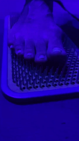 Person stands on nail bed at neon-lit party