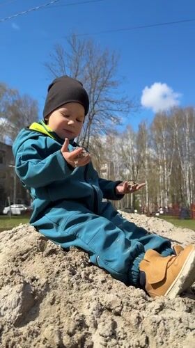 Child plays in sand pile under clear skies in Yaroslavl