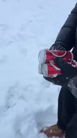 The video shows a gloved person dropping four cans into the snow, where three come to rest. The cans are red and labelled in a different language, with the name "FORTUNA" visible on some of them. The snow is fresh, white, and unmarked except for some footprints.  The person throwing the cans is wearing a dark jacket. The video is shot from a first-person perspective, and the wind is audible.