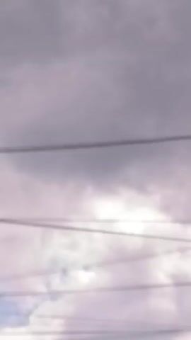The video captures a cloudy sky with several power lines strung across the frame. A street lamp with a curved pole and an ovular light fixture is visible in the lower right quadrant. The sky is overcast with various shades of grey clouds, suggesting potentially inclement weather. The power lines appear to be a significant element of the scene, running horizontally through the shot. The overall impression is one of an outdoor environment under a dull sky, with man-made infrastructure dominating the view.