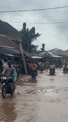 Motorcycles navigate heavy flooding on a rainy Ihiagwa street.