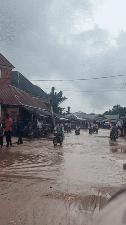 Motorcycles navigate heavy flooding on a rainy Ihiagwa street.