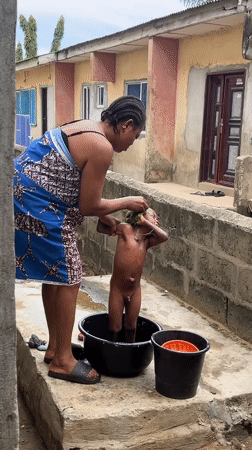 Woman bathes child outdoors in Badagry, Nigeria