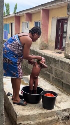 Woman bathes child outdoors in Badagry, Nigeria