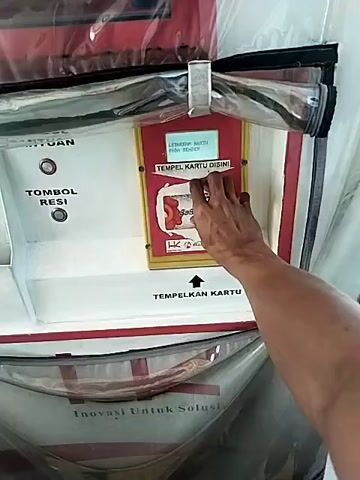 A person inserts a card into a toll machine, then the boom lifts up. The video then cuts to a view from inside a car. The car is approaching a tollbooth. A person is walking on the shoulder of the road ahead. After the car passes, the tollbooth is visible. It's red and white and encased in a plastic sheet.