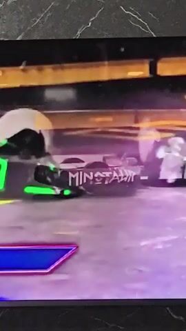 The video shows a robot combat event. Two robots are engaged in a match. One robot, labeled "MINOTAUR", is dark with white lettering. The other robot is partially obscured but has green accents. They are in an arena with orange walls and a purple floor. Sparks and debris are visible as the robots collide. A "REPLAY" banner is displayed on the screen.