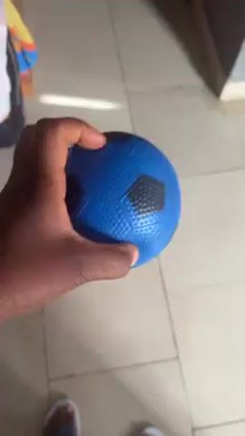 A person is holding a blue ball with black spots and tapping it on a tiled floor. The person is wearing white flip-flops.  The camera angle is a close-up and moves to follow the ball.