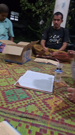 Outdoor evening reading circle on woven mats in rural Indonesia