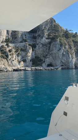 Boat travels Capri coastline on clear morning