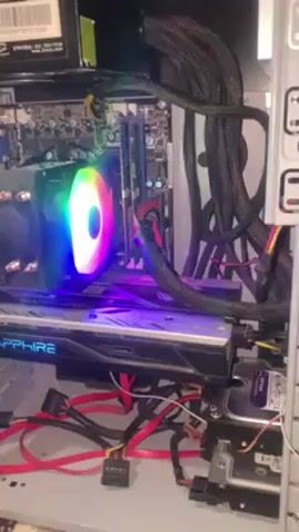 The inside of a desktop computer case is shown. A rainbow-colored CPU cooler sits atop the motherboard. Below it, a Sapphire-branded graphics card spans the width of the case. Various red and black power cables snake through the interior, connecting components. A hard drive is mounted on the right side of the case. The overall arrangement appears functional, if a bit cluttered with cables.