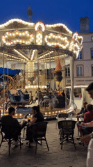 Evening cafe crowds gather around carousel in Metz square