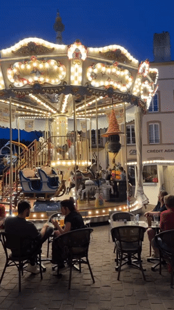 Evening cafe crowds gather around carousel in Metz square