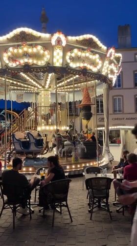 Evening cafe crowds gather around carousel in Metz square