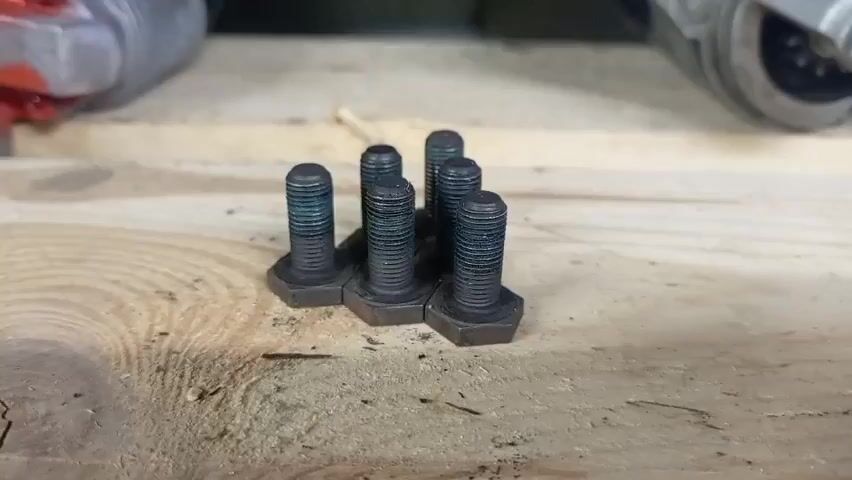 The video pans across a wooden shelf displaying a collection of automotive starter motors. In the foreground, a small cluster of hex-head bolts with a dark, possibly bluish coating, lies on the shelf. The starter motors are arranged in rows, most appearing to be made of silver-colored metal with some red accents. The lighting suggests an indoor setting, likely a storage or workshop area.