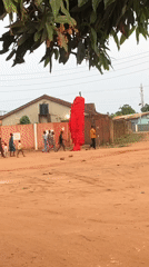 Rural village procession features tall red structure on dirt road