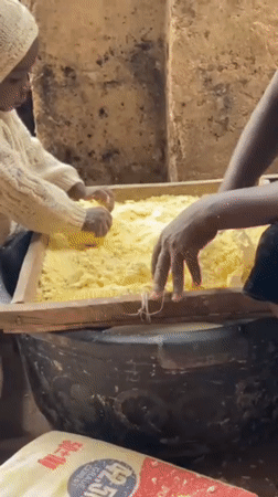 Child helps adults process grain in Nigerian community operation