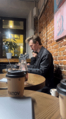 Man works on laptop in café while woman sits nearby