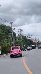 Pink Jeep on a cloudy, wire-lined road with traffic