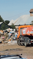 Orange tanker truck wets down a garbage pile in Shymkent