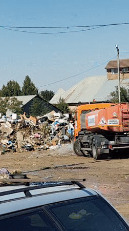 Orange tanker truck wets down a garbage pile in Shymkent