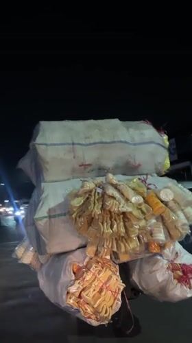 Heavily loaded motorcycle travels Tangerang road at night