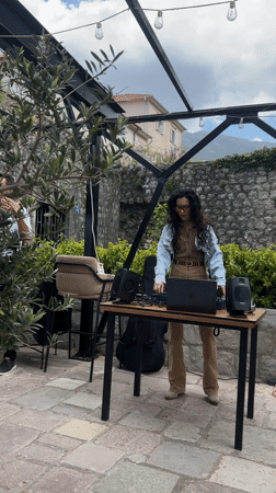 Woman DJs outdoors with laptop setup in Dobrota, Montenegro