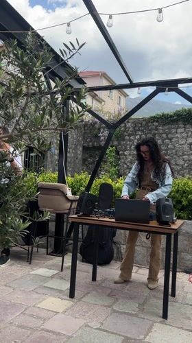 Woman DJs outdoors with laptop setup in Dobrota, Montenegro