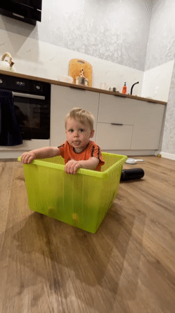 Toddler plays inside a bright green plastic bin indoors