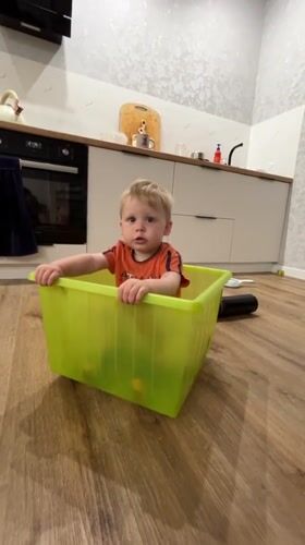 Toddler plays inside a bright green plastic bin indoors