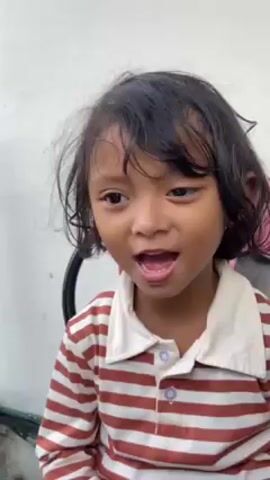 A young girl with short, dark hair, wearing a red and white striped shirt with a white collar, looks at the camera and smiles. She then opens her mouth and laughs widely. The background is a white wall.