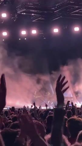 The video shows a concert crowd. The stage is lit with pink lights and smoke. People are holding up their hands. A banner across the top of the stage reads "OPEN'ER FESTIVAL". The camera is positioned within the crowd, looking towards the stage.