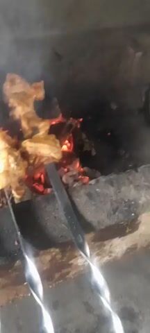 The video shows meat cooking on skewers over hot coals. The meat is browned and appears to be chicken. Smoke is rising from the grill, obscuring some of the details. The video is shaky and the focus is not always sharp. The overall impression is one of food being prepared outdoors, likely for a meal.