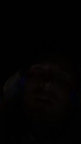 The video shows a person’s face in the dark.  The person is wearing headphones.