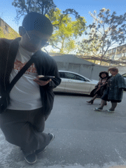 Man checks phone on urban sidewalk amid pedestrian traffic