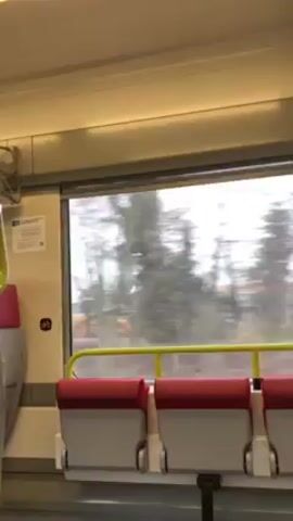 The video shows an interior view from a moving train. The camera looks towards the window, displaying a blurred view of trees and buildings passing by. The seats in the train are red and gray.
