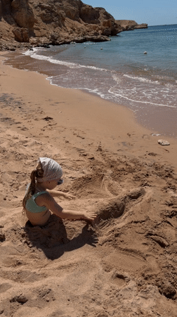 Child plays buried in sand on Sharm El Sheikh beach