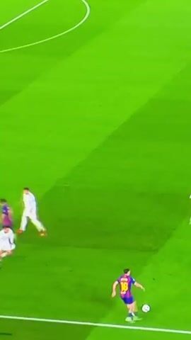 The video shows a soccer match on a green field. There are multiple players visible, some wearing white uniforms and others wearing blue and red. One player wearing the number 10 is dribbling the ball. There is also a referee wearing a yellow and black uniform. The camera angle is high, giving an overview of the players and the field.