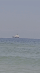 Cargo ships offshore as swimmers enjoy Ashkelon's calm morning beach