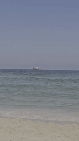Cargo ships offshore as swimmers enjoy Ashkelon's calm morning beach