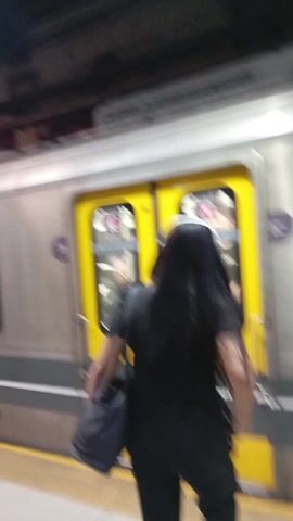 A shaky handheld video shows people boarding and exiting a subway car at a station.  The subway car is silver with a yellow door. People are entering and exiting the car.  The station platform is visible through the open door.  A man with glasses and a blue backpack exits the train. Another person enters. Passengers are seated inside the train.