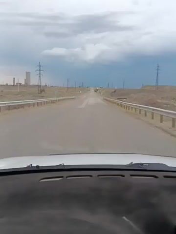 The video shows a road from the perspective of a car driving forward. There are power lines on both sides of the road and distant industrial structures. The sky is cloudy. The audio contains spoken French phrases.